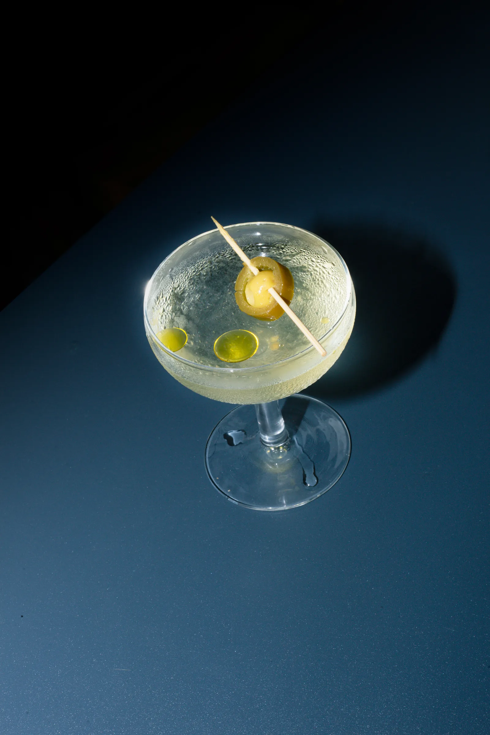 Martini con aceitunas sobre mesa azul marino